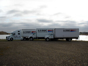 Two shiny, new, white freight trucks with a matching tractor-trailer unit in the background is part of the Leduc Truck Service modern fleet.